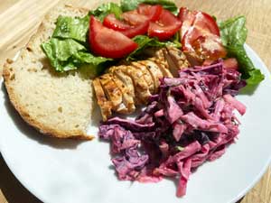 A plate with salad, a slice of homemade bread, bbq chicken and a colourful beetroot coleslaw