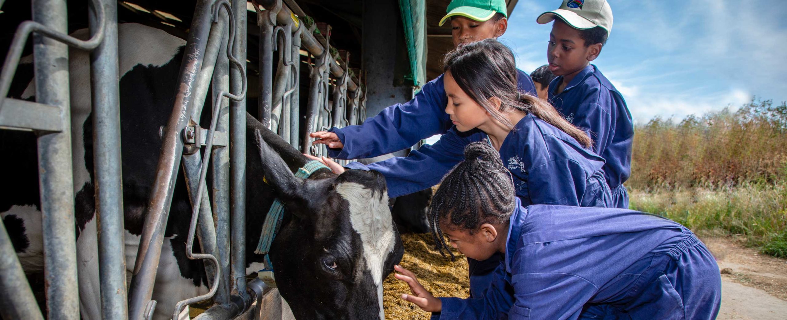 Children in Farms for City Children overalls with a cow peeping out of a barn
