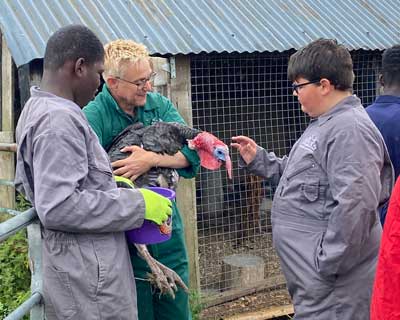 Young people from a visiting community group with a Farms for City Children staff member holding a turkey.