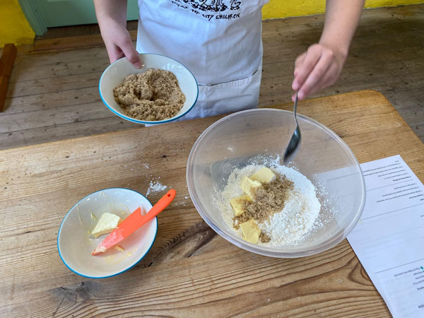 A child's hands putting sugar into a bowl of flour and butter.
