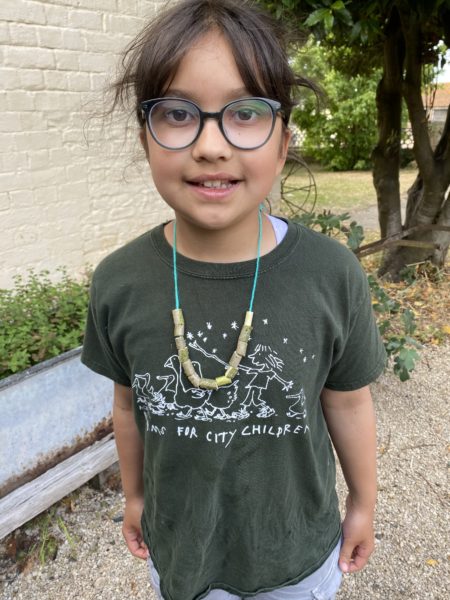 Child in Farms for City Children t-shirt holding up an Elder bead necklace