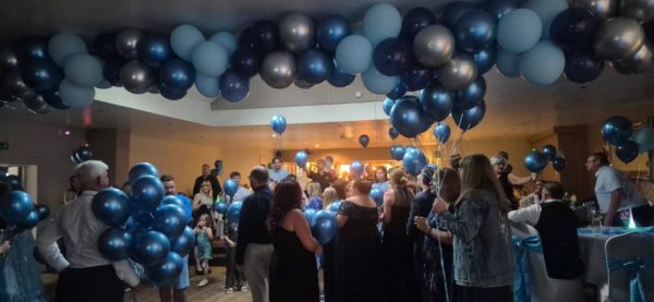a wide shot in a conference room of a crowd, backs to camera and a ceiling full of blue balloons