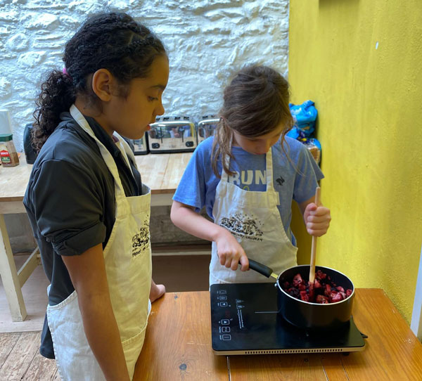Two young people stirring a saucepan of fruit on an induction hob