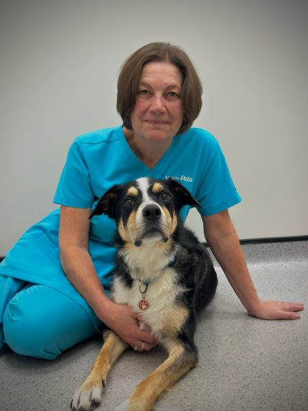 Lou in her turquoise vet uniform sat with a mixed breed dog