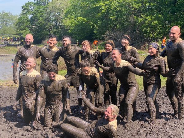 a group of 15 staff of BOM in a muddy field, covered top to toe in mud