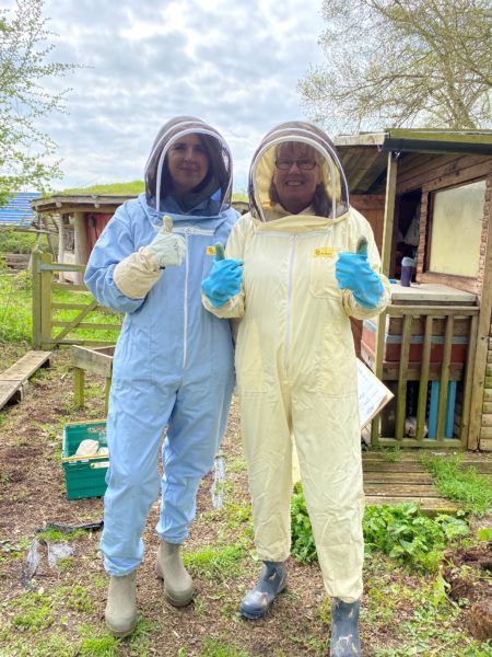 Tracy on the right in a pale lemon bee keeping outfit with Sarah from John Horseman Trust who is in a blue bee keeping outfit stood outdoors with their thumbs up