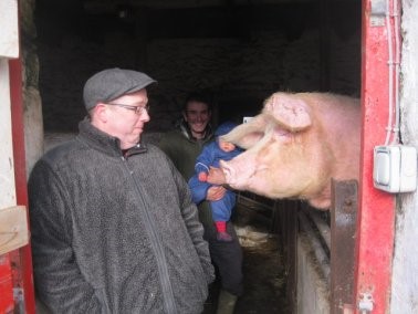 Matt in a grey coat and cap laughing at a pig as it leans towards him