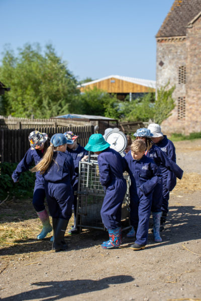 a group of children are moving a weighing machine together. All dressed in navy overalls