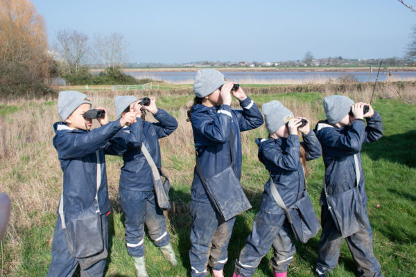 Group of students in navy FfCC waterproofs looking to the distance with binoculars