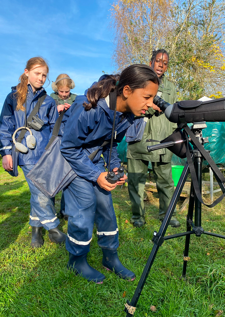 Group of children in farm overalls outdoors looking through telescope.