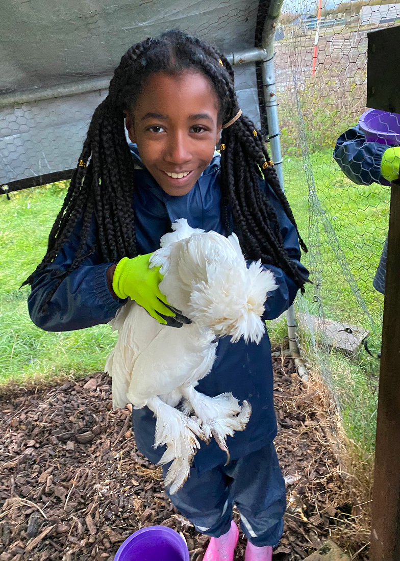 School child in overalls holding a chicken on a farm residential