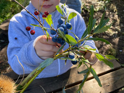 Child's hands adding berry decorations to a willow crown.