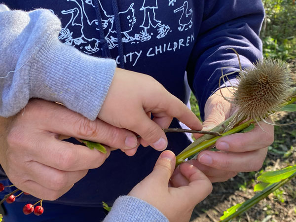 Child's hands weaving willow along with the hands of an adult's hands in a farms for city children sweatshirt