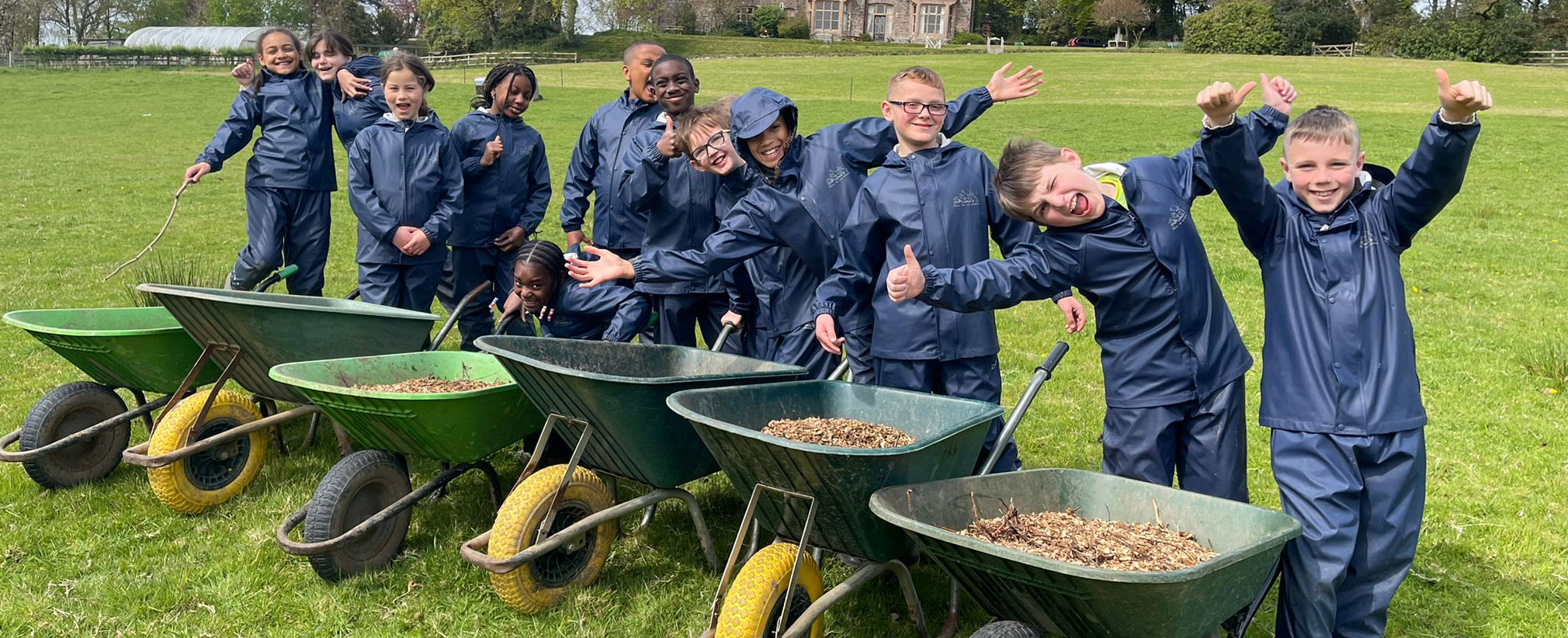Group of school children in front of nethercott house farm with wheelbarrows.